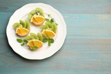 Photo of Delicious dessert. Tartlets with fruits and mint on light blue wooden table, top view. Space for text