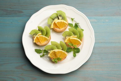 Photo of Tartlets with fruits and mint on light blue wooden table, top view. Delicious dessert