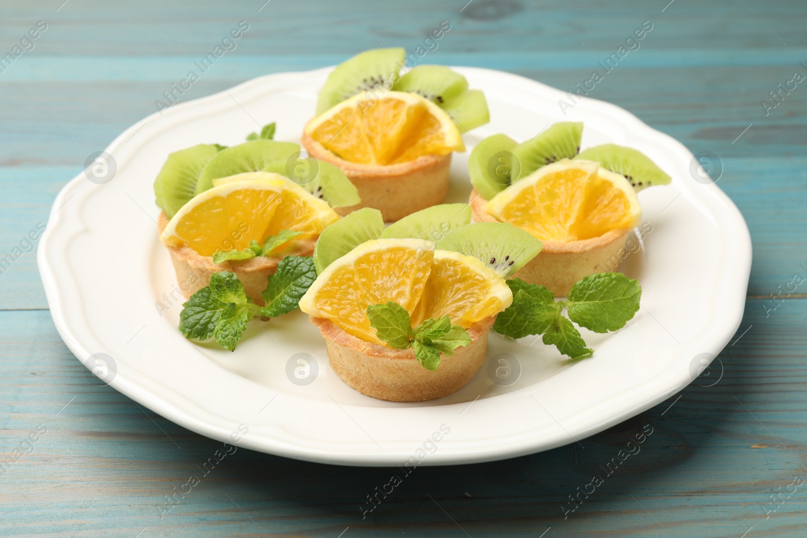 Tartlets with fruits and mint on light blue wooden table, closeup. Delicious dessert Photo of Tartlets with fruits and mint on light blue wooden table, closeup. Delicious dessert