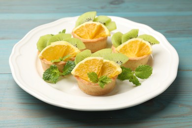 Photo of Tartlets with fruits and mint on light blue wooden table, closeup. Delicious dessert