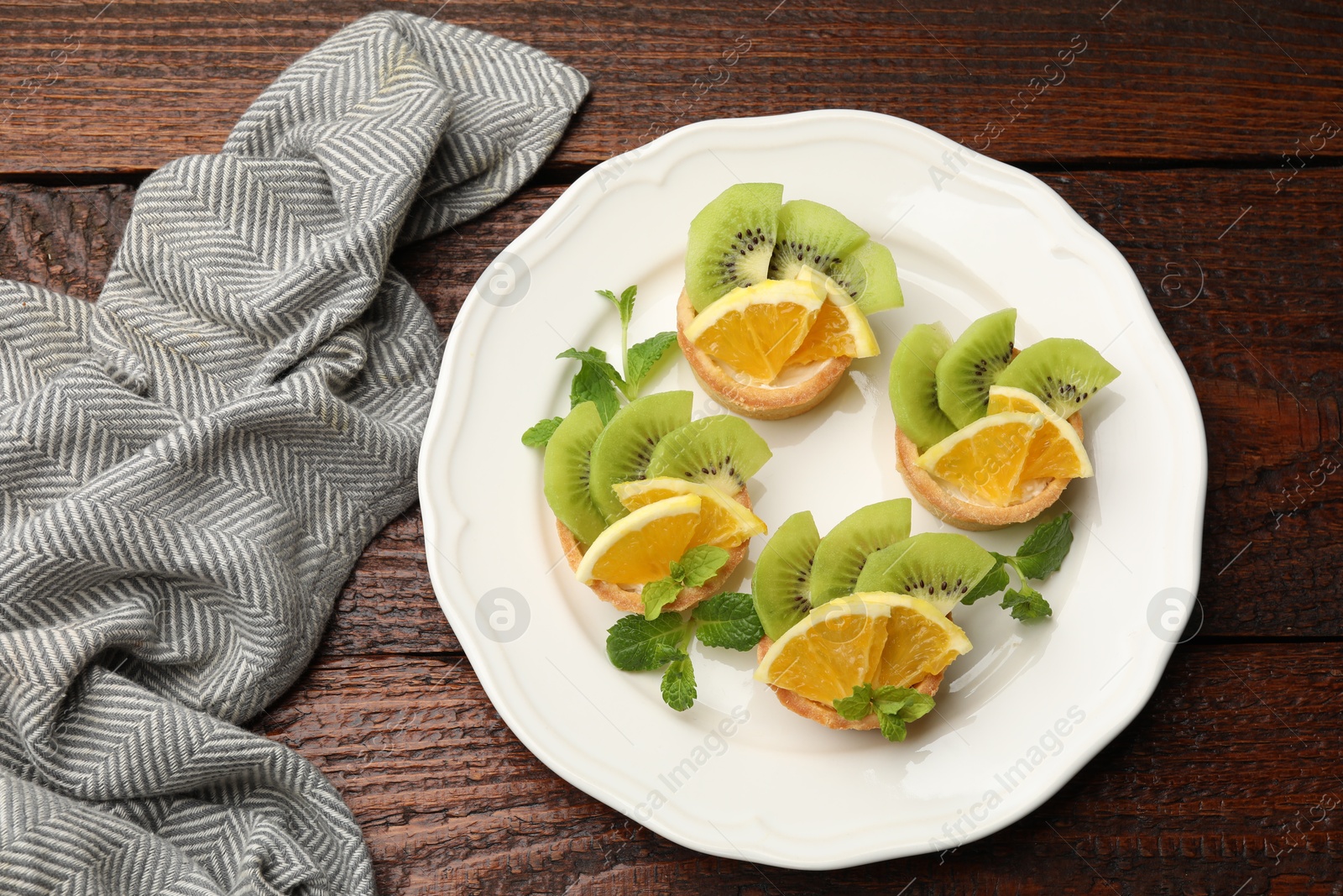 Tartlets with fruits and mint on wooden table, top view. Delicious dessert Photo of Tartlets with fruits and mint on wooden table, top view. Delicious dessert