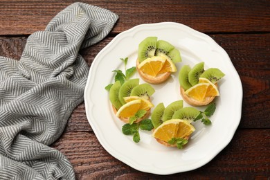 Photo of Tartlets with fruits and mint on wooden table, top view. Delicious dessert