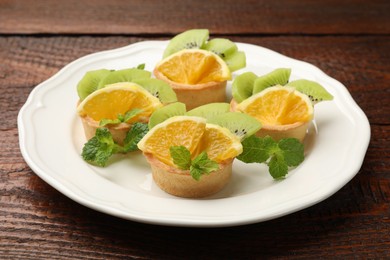 Photo of Tartlets with fruits and mint on wooden table, closeup. Delicious dessert