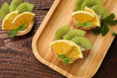 Photo of Tartlets with fruits and mint on wooden table, flat lay. Delicious dessert