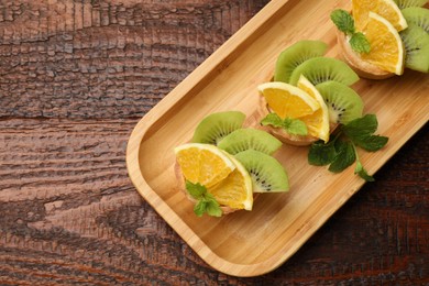 Photo of Delicious dessert. Tartlets with fruits and mint on wooden table, top view. Space for text