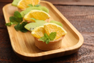 Photo of Tartlets with fruits and mint on wooden table, closeup. Delicious dessert