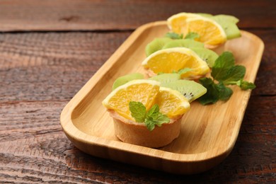 Photo of Tartlets with fruits and mint on wooden table, closeup. Delicious dessert