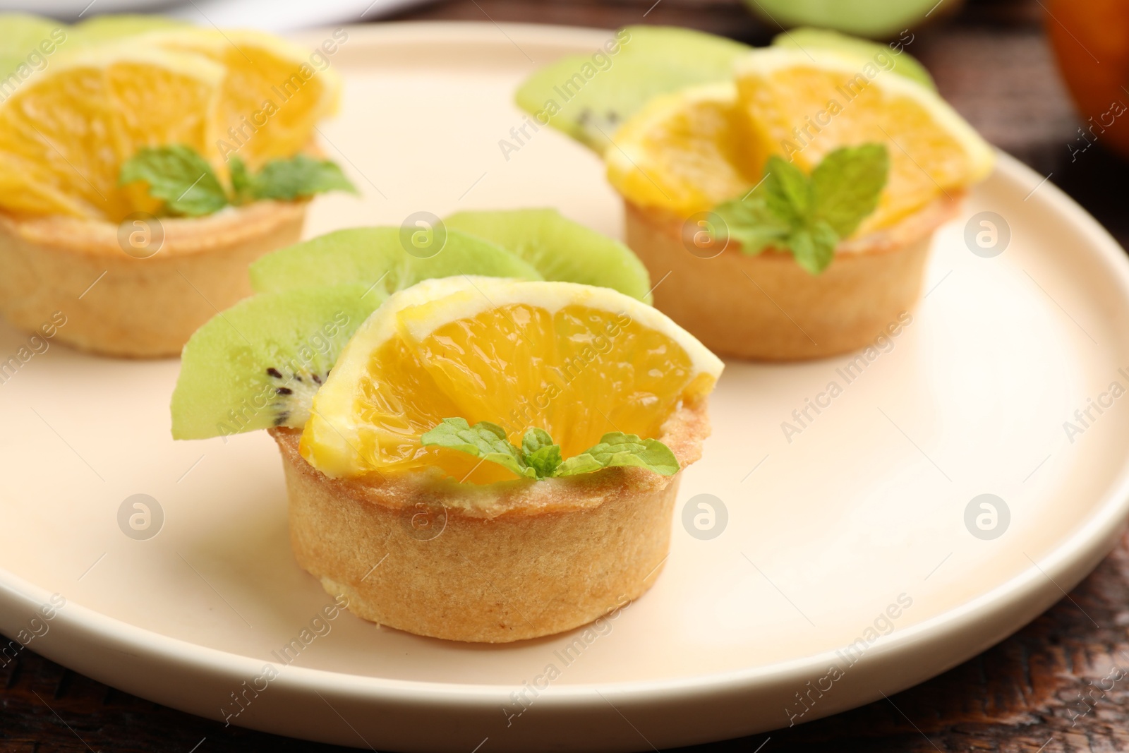 Tartlets with fruits and mint on table, closeup. Delicious dessert Photo of Tartlets with fruits and mint on table, closeup. Delicious dessert
