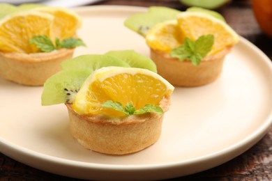 Photo of Tartlets with fruits and mint on table, closeup. Delicious dessert