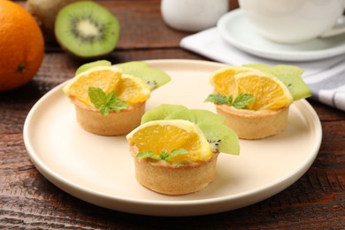 Photo of Tartlets with fruits and mint on wooden table, closeup. Delicious dessert