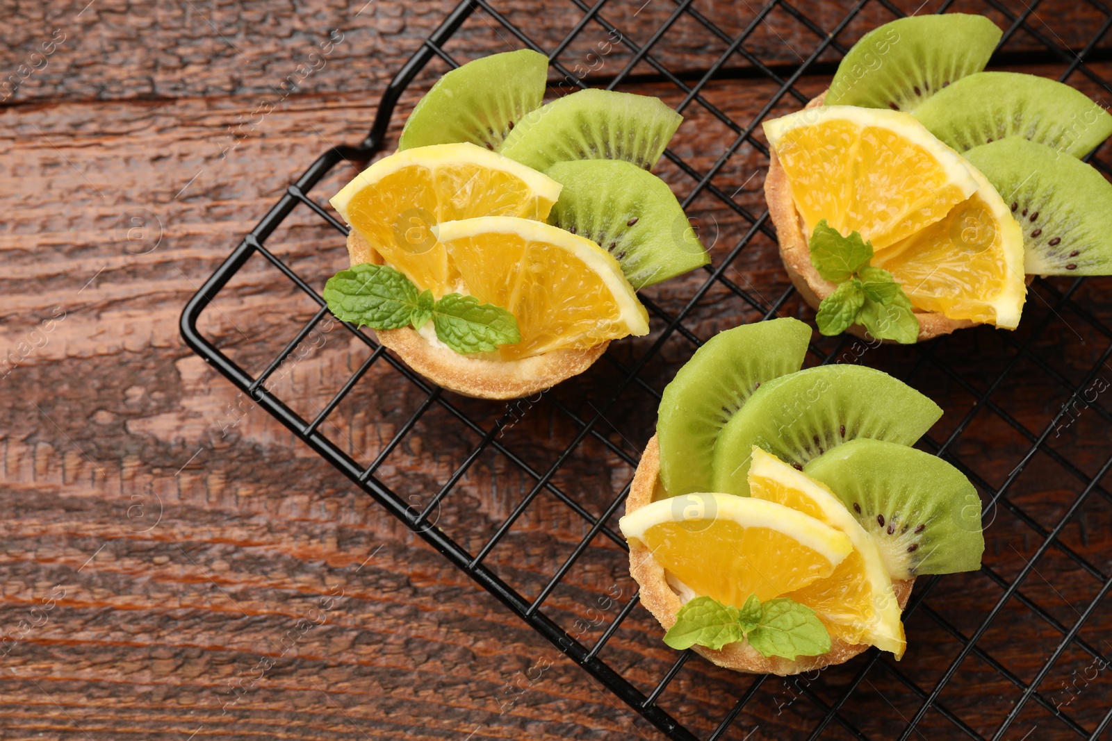 Tartlets with fruits and mint on wooden table, top view. Delicious dessert Photo of Tartlets with fruits and mint on wooden table, top view. Delicious dessert