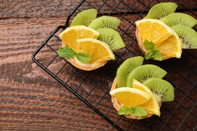 Photo of Tartlets with fruits and mint on wooden table, top view. Delicious dessert