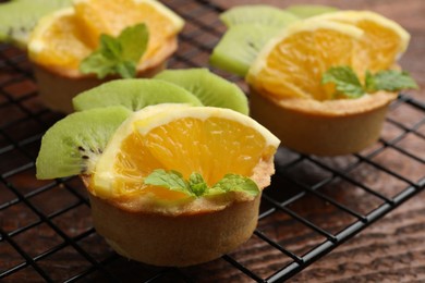 Photo of Tartlets with fruits and mint on wooden table, closeup. Delicious dessert