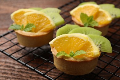 Photo of Tartlets with fruits and mint on wooden table, closeup. Delicious dessert