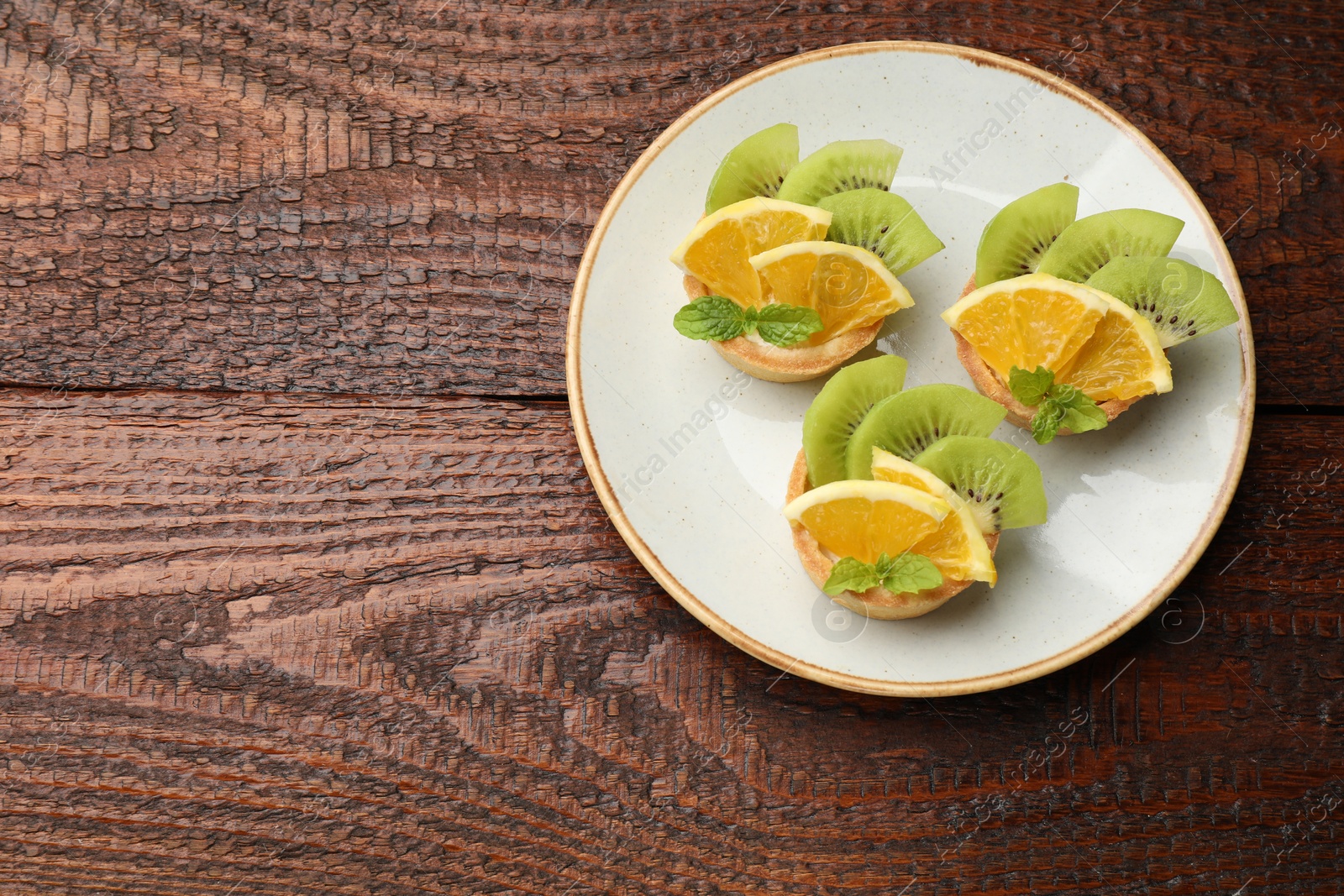 Delicious dessert. Tartlets with fruits and mint on wooden table, top view. Space for text Photo of Delicious dessert. Tartlets with fruits and mint on wooden table, top view. Space for text
