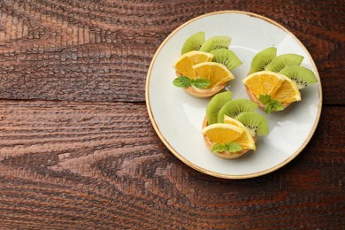 Photo of Delicious dessert. Tartlets with fruits and mint on wooden table, top view. Space for text