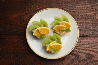 Photo of Tartlets with fruits and mint on wooden table, top view. Delicious dessert