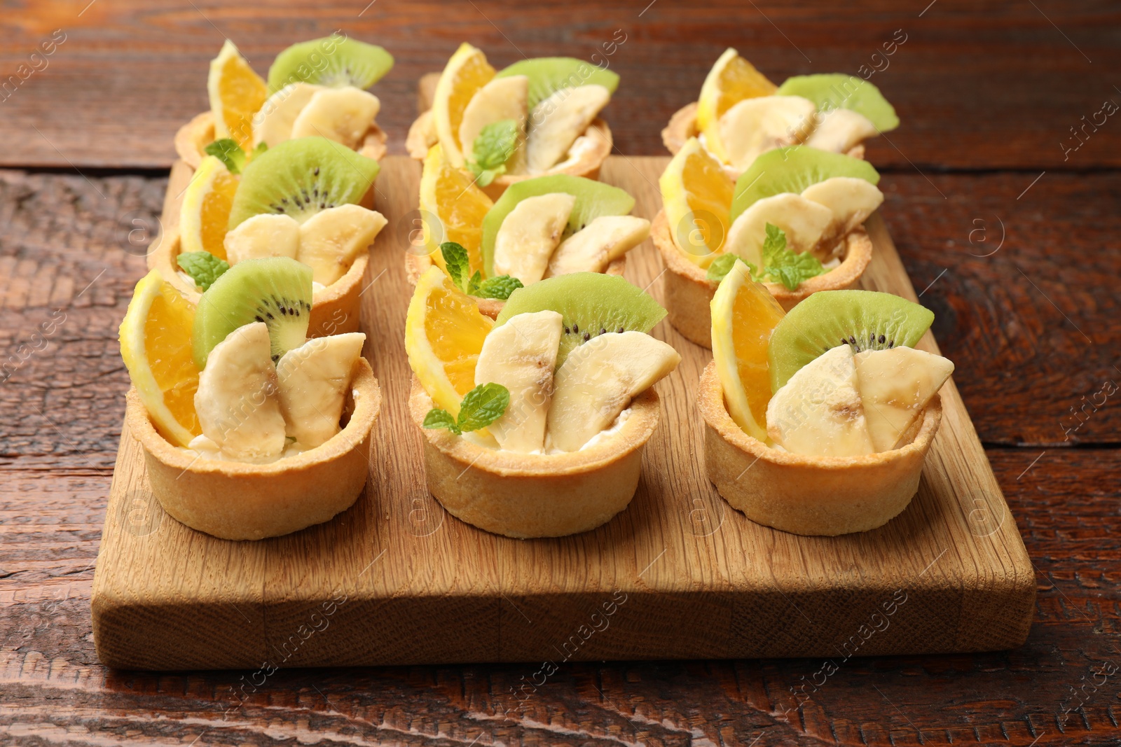 Tartlets with fruits and mint on wooden table, closeup. Delicious dessert Photo of Tartlets with fruits and mint on wooden table, closeup. Delicious dessert