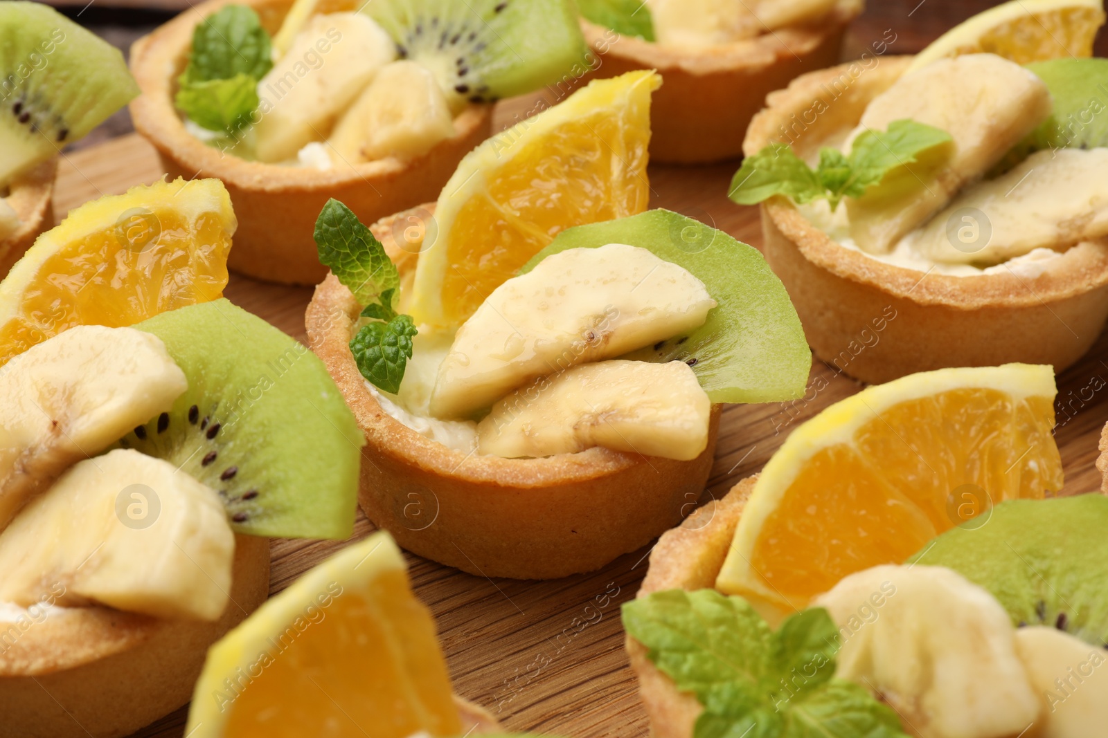 Tartlets with fruits and mint on wooden board, closeup. Delicious dessert Photo of Tartlets with fruits and mint on wooden board, closeup. Delicious dessert