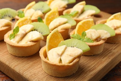 Photo of Tartlets with fruits and mint on table, closeup. Delicious dessert