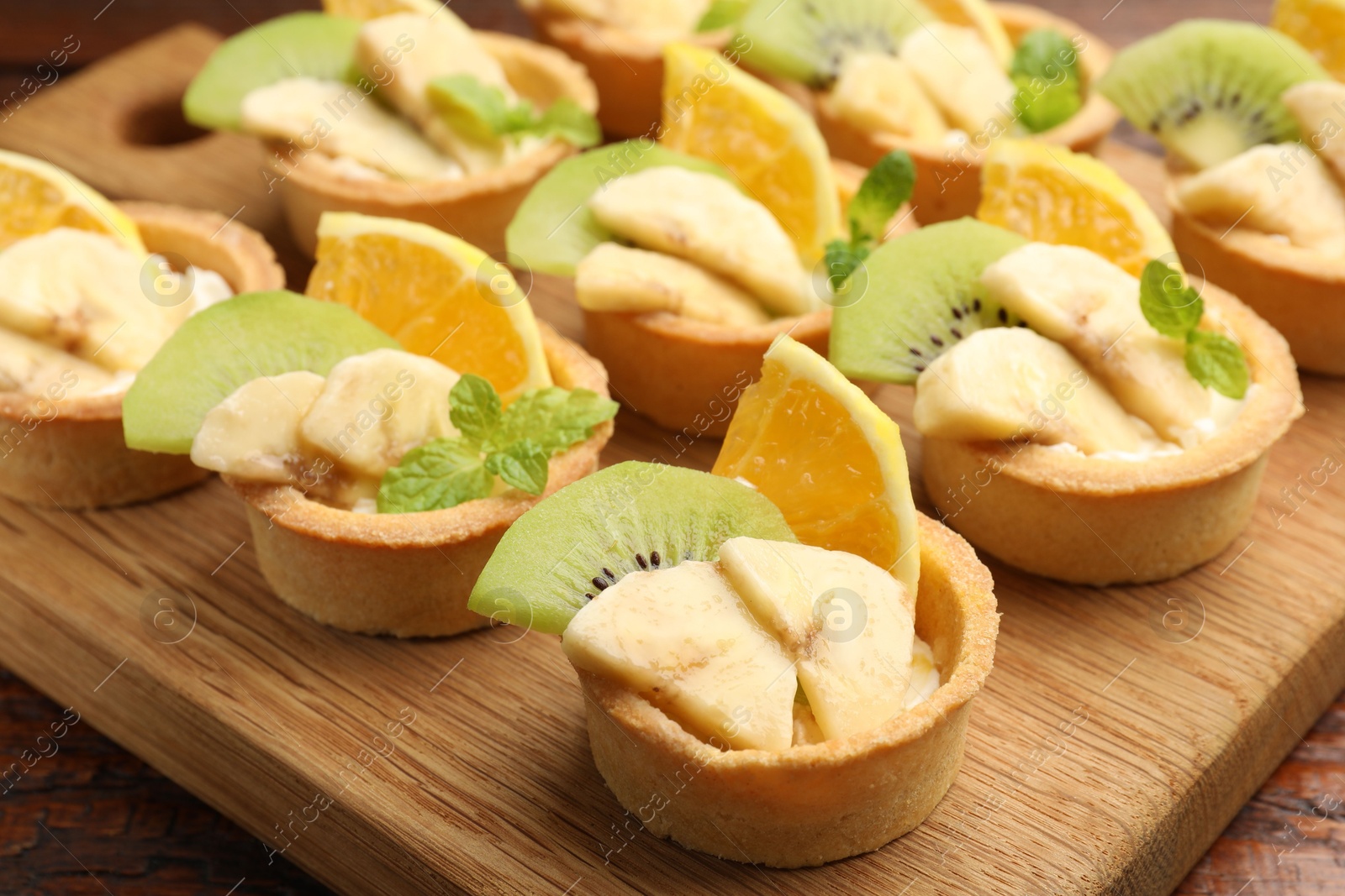 Tartlets with fruits and mint on table, closeup. Delicious dessert Photo of Tartlets with fruits and mint on table, closeup. Delicious dessert
