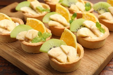 Photo of Tartlets with fruits and mint on table, closeup. Delicious dessert