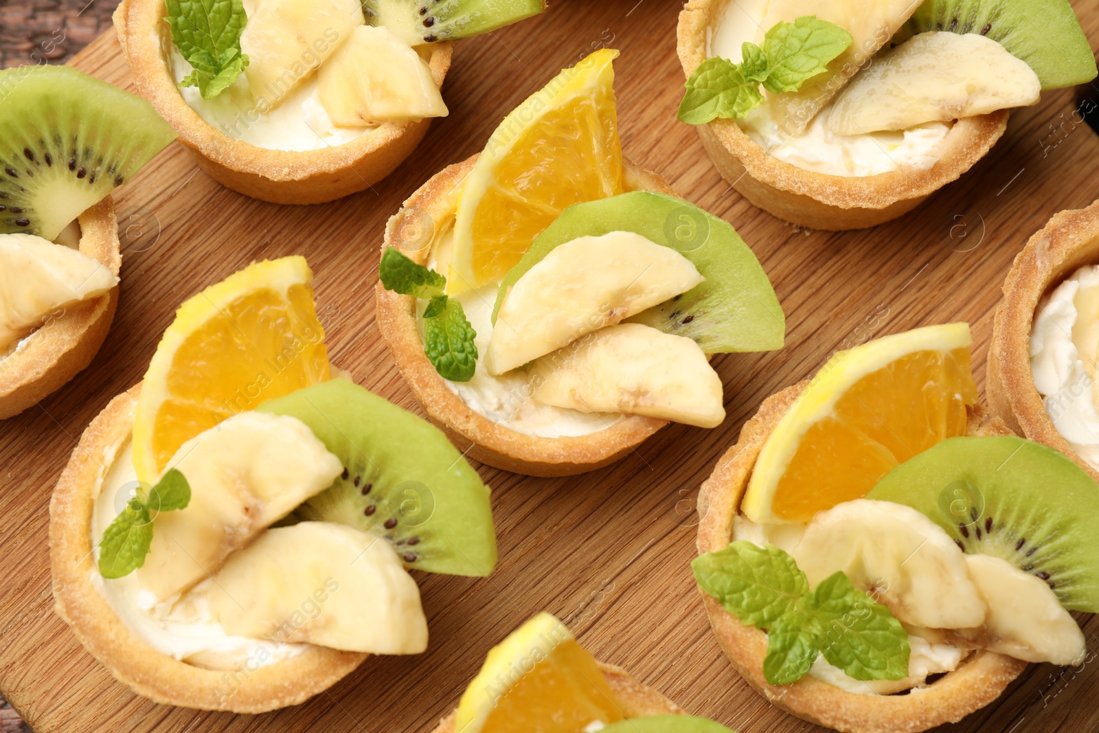 Tartlets with fruits and mint on wooden board, flat lay. Delicious dessert Photo of Tartlets with fruits and mint on wooden board, flat lay. Delicious dessert
