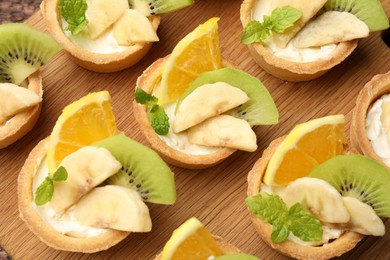 Photo of Tartlets with fruits and mint on wooden board, flat lay. Delicious dessert
