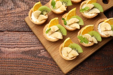 Photo of Delicious dessert. Tartlets with fruits and mint on wooden table, top view. Space for text