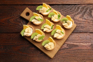Photo of Tartlets with fruits and mint on wooden table, top view. Delicious dessert