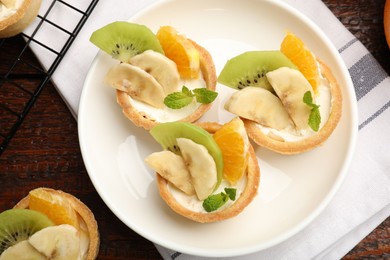 Photo of Tartlets with fruits and mint on wooden table, flat lay. Delicious dessert