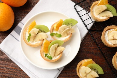 Photo of Tartlets with fruits and mint on wooden table, flat lay. Delicious dessert