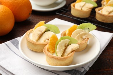 Photo of Tartlets with fruits and mint on wooden table, closeup. Delicious dessert