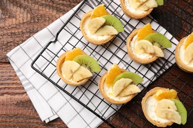 Photo of Tartlets with fruits and mint on wooden table, top view. Delicious dessert