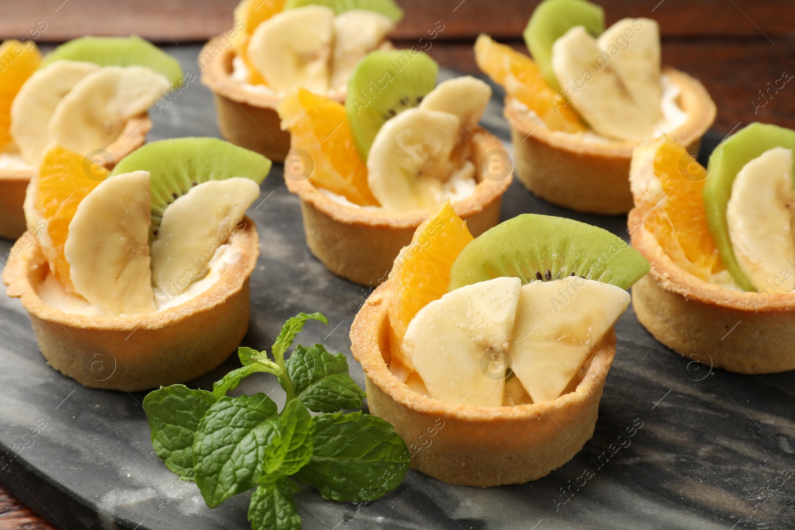 Tartlets with fruits and mint on table, closeup. Delicious dessert Photo of Tartlets with fruits and mint on table, closeup. Delicious dessert