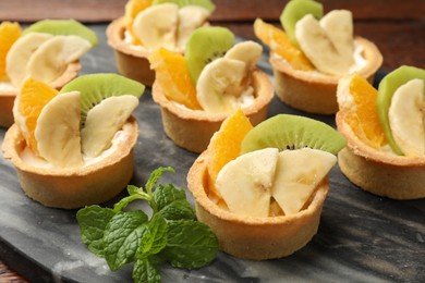 Photo of Tartlets with fruits and mint on table, closeup. Delicious dessert