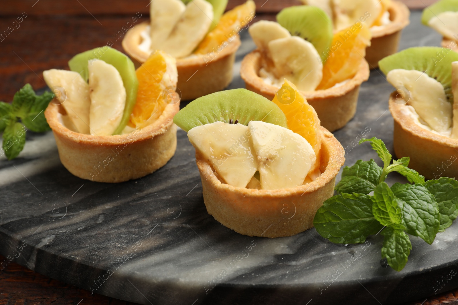 Tartlets with fruits and mint on table, closeup. Delicious dessert Photo of Tartlets with fruits and mint on table, closeup. Delicious dessert