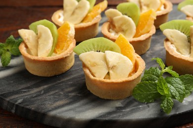 Photo of Tartlets with fruits and mint on table, closeup. Delicious dessert
