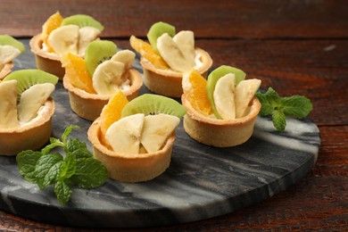 Photo of Tartlets with fruits and mint on wooden table, closeup. Delicious dessert