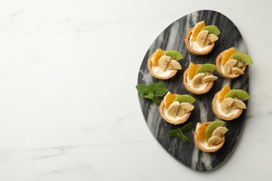 Photo of Delicious dessert. Tartlets with fruits and mint on white marble table, flat lay. Space for text