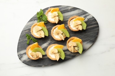 Photo of Tartlets with fruits and mint on white marble table, flat lay. Delicious dessert