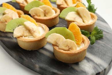 Photo of Tartlets with fruits and mint on white table, closeup. Delicious dessert