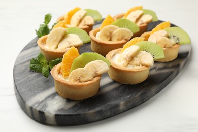 Photo of Tartlets with fruits and mint on white marble table, closeup. Delicious dessert