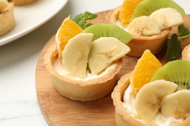 Photo of Tartlets with fruits and mint on white marble table, closeup. Delicious dessert