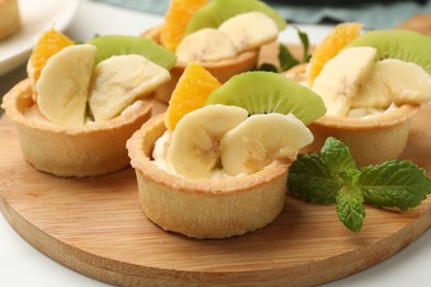 Photo of Tartlets with fruits and mint on table, closeup. Delicious dessert