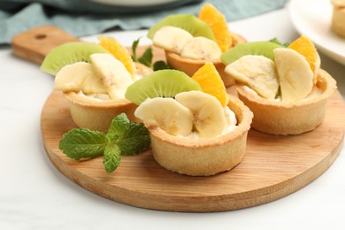 Photo of Tartlets with fruits and mint on white table, closeup. Delicious dessert