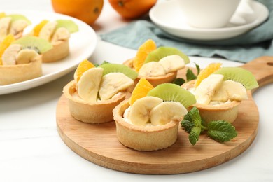 Photo of Tartlets with fruits and mint on white marble table, closeup. Delicious dessert