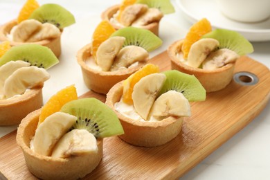 Photo of Tartlets with fruits on white table, closeup. Delicious dessert