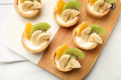 Photo of Tartlets with fruits on white table, top view. Delicious dessert