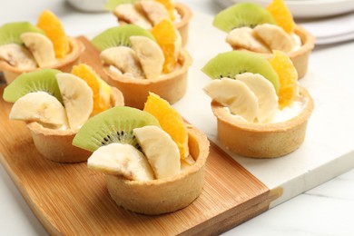 Photo of Tartlets with fruits on white marble table, closeup. Delicious dessert